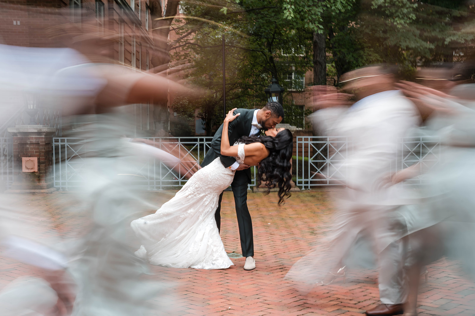 Couple dip kiss with motion blur bridesmaids brick courtyard