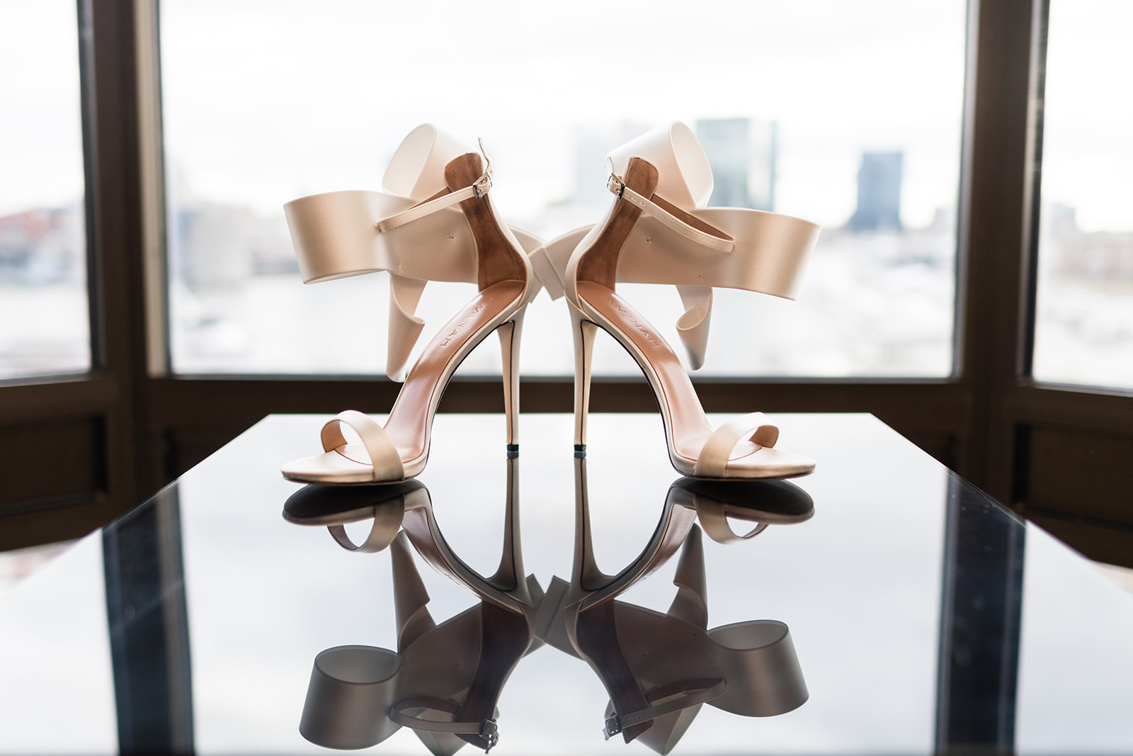 Blush stiletto heels on glass table with reflection