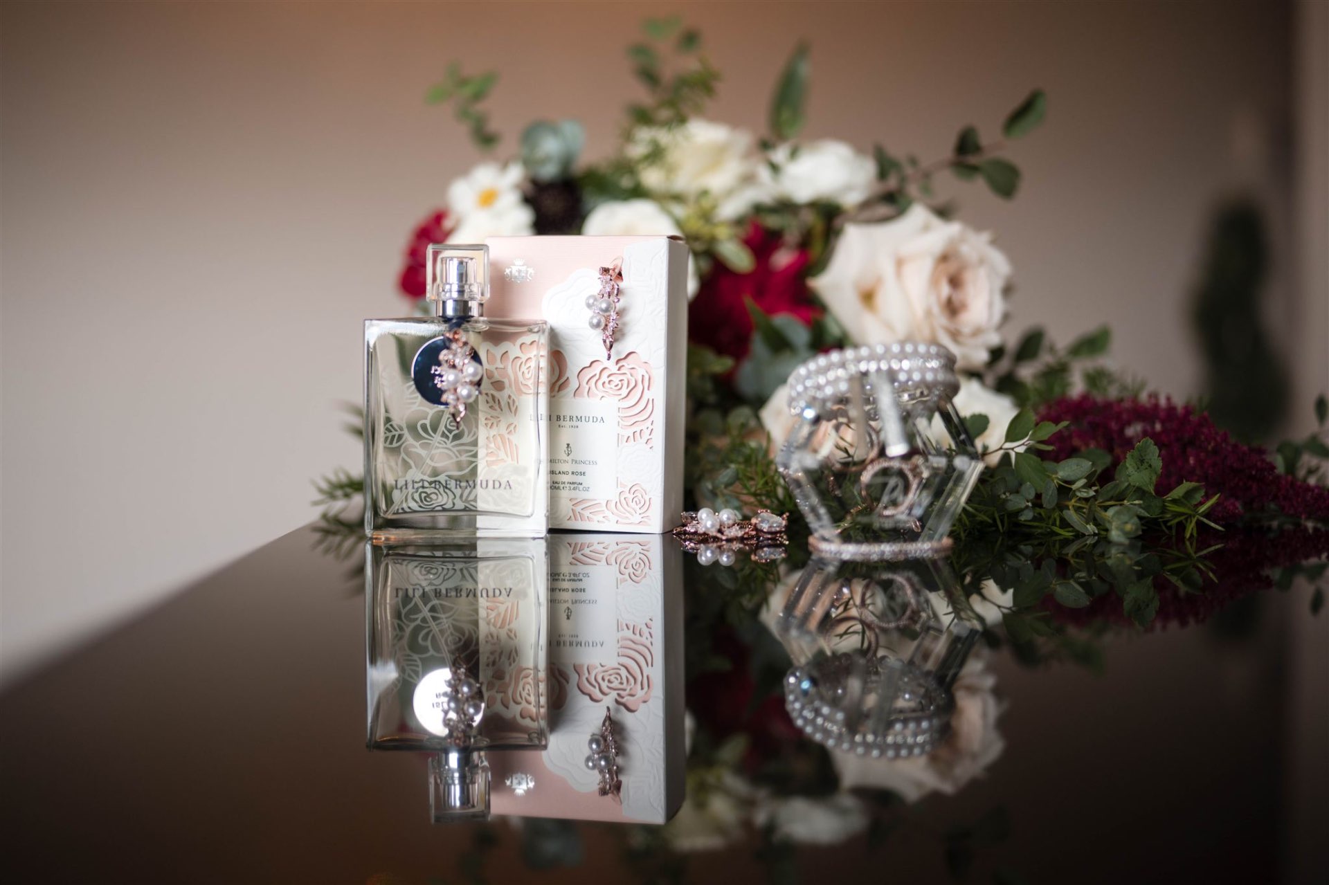 Bridal perfume earrings and bouquet on glass reflection