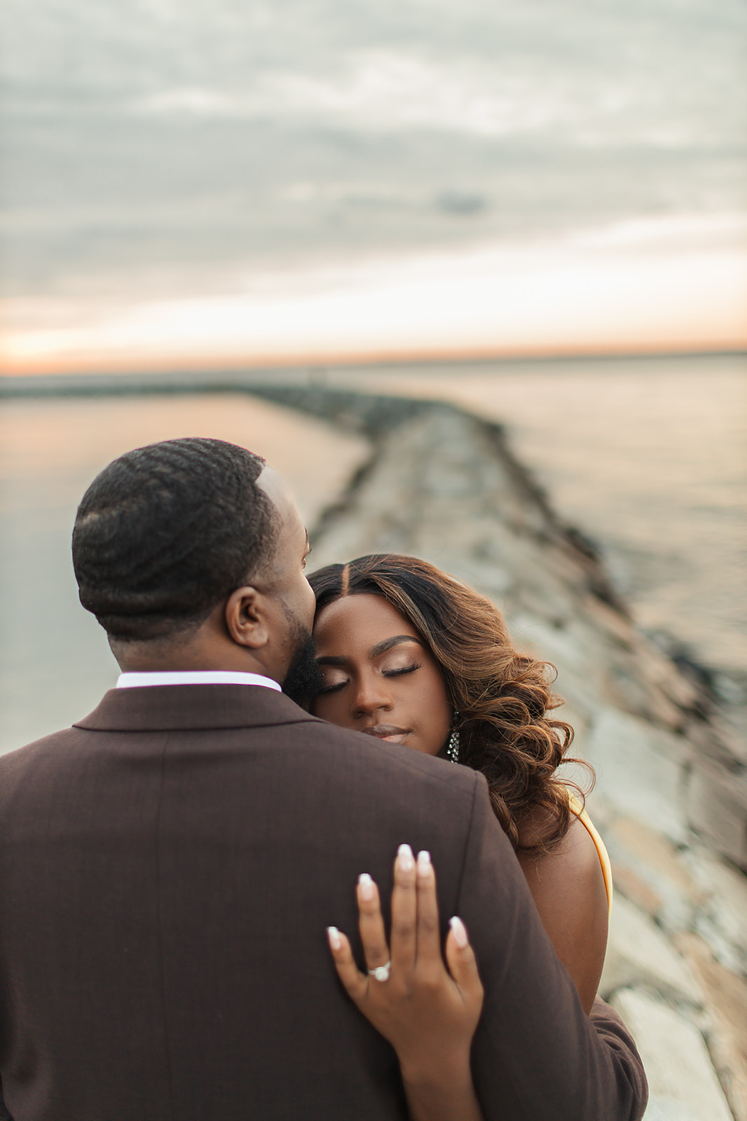 Couple embrace on jetty at sunset over ocean