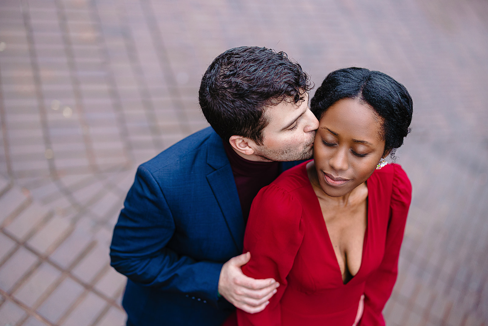Couple kiss from overhead by brick wall in red dress