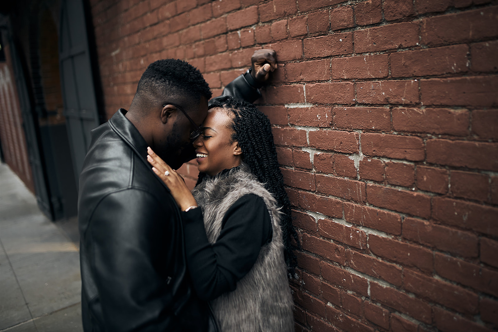 Couple laughing by brick wall in leather jacket
