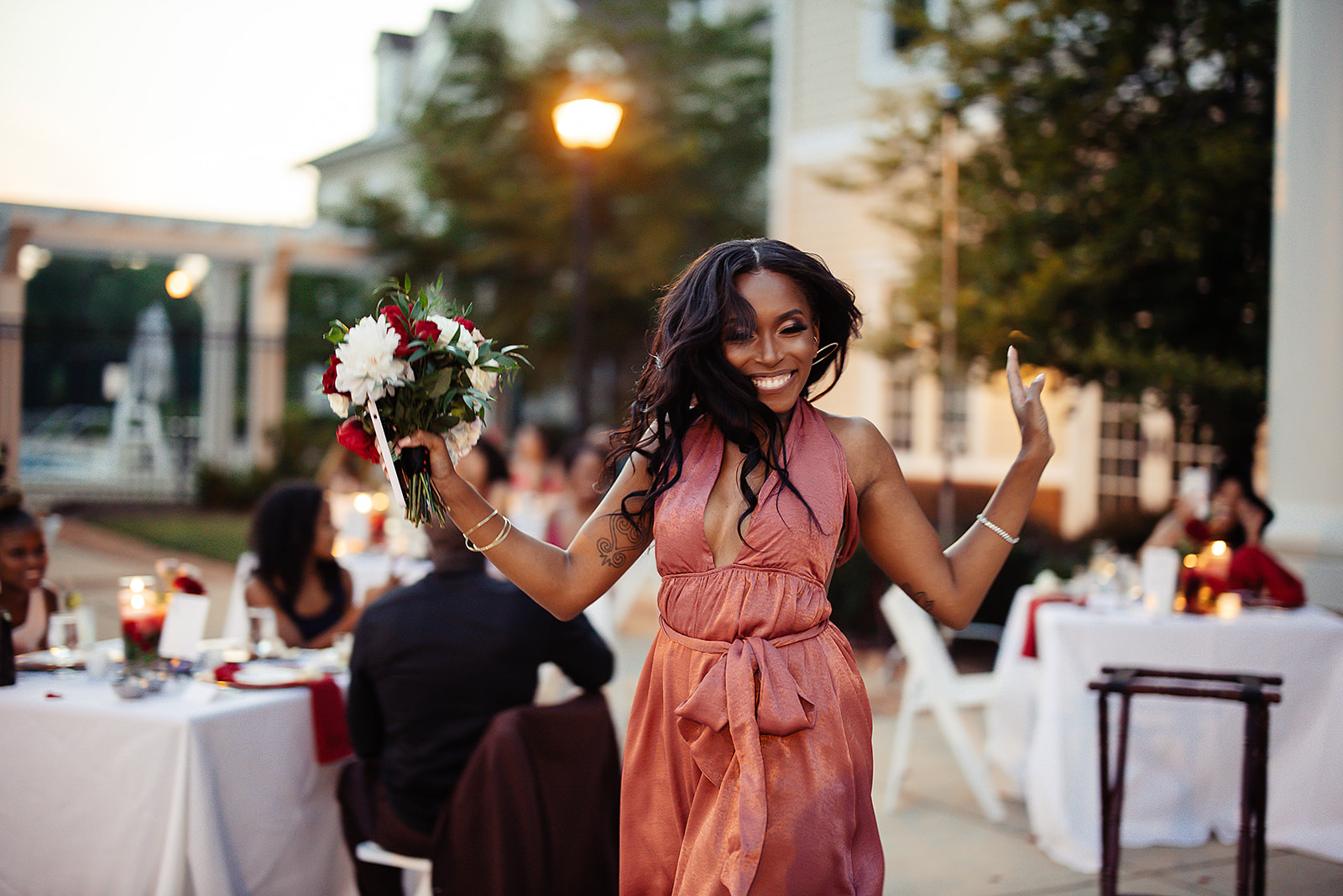 Guest catching bouquet in coral halter dress at outdoor reception
