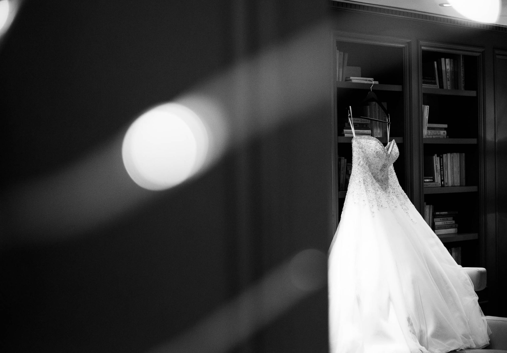 Wedding dress hanging by bookshelf black and white bokeh