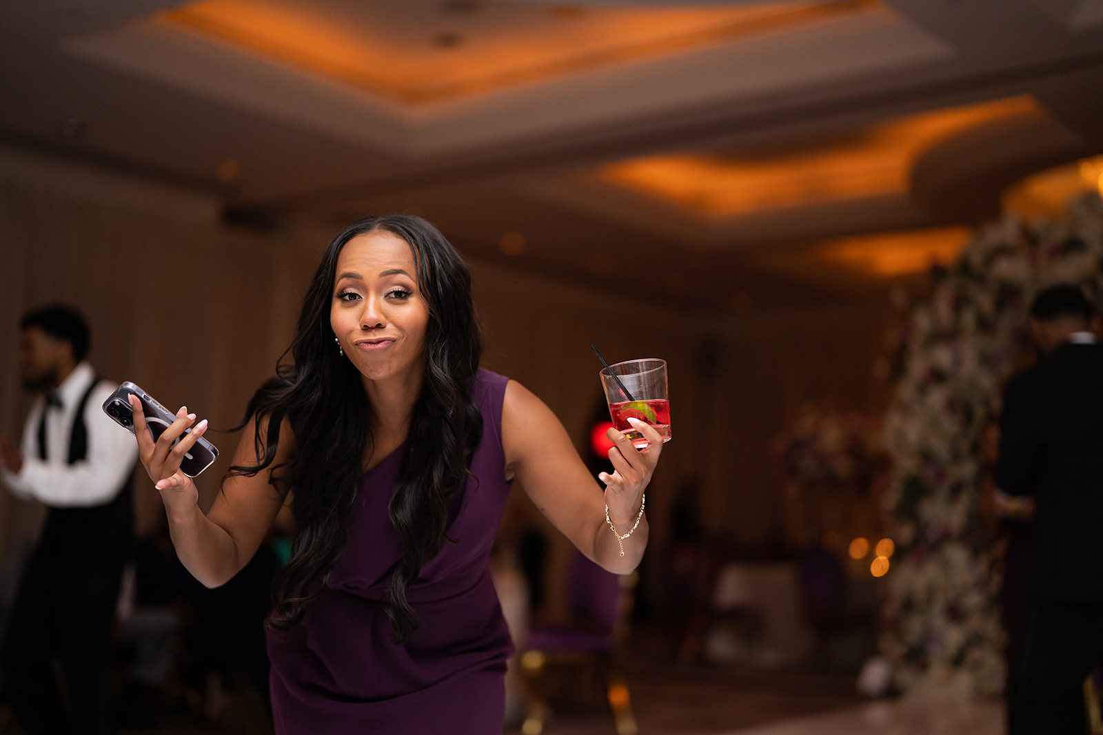 Guest with cocktail and phone in purple dress at reception candid