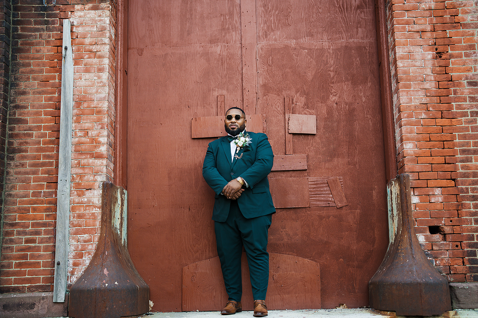 Groom in teal suit with sunglasses brick warehouse portrait
