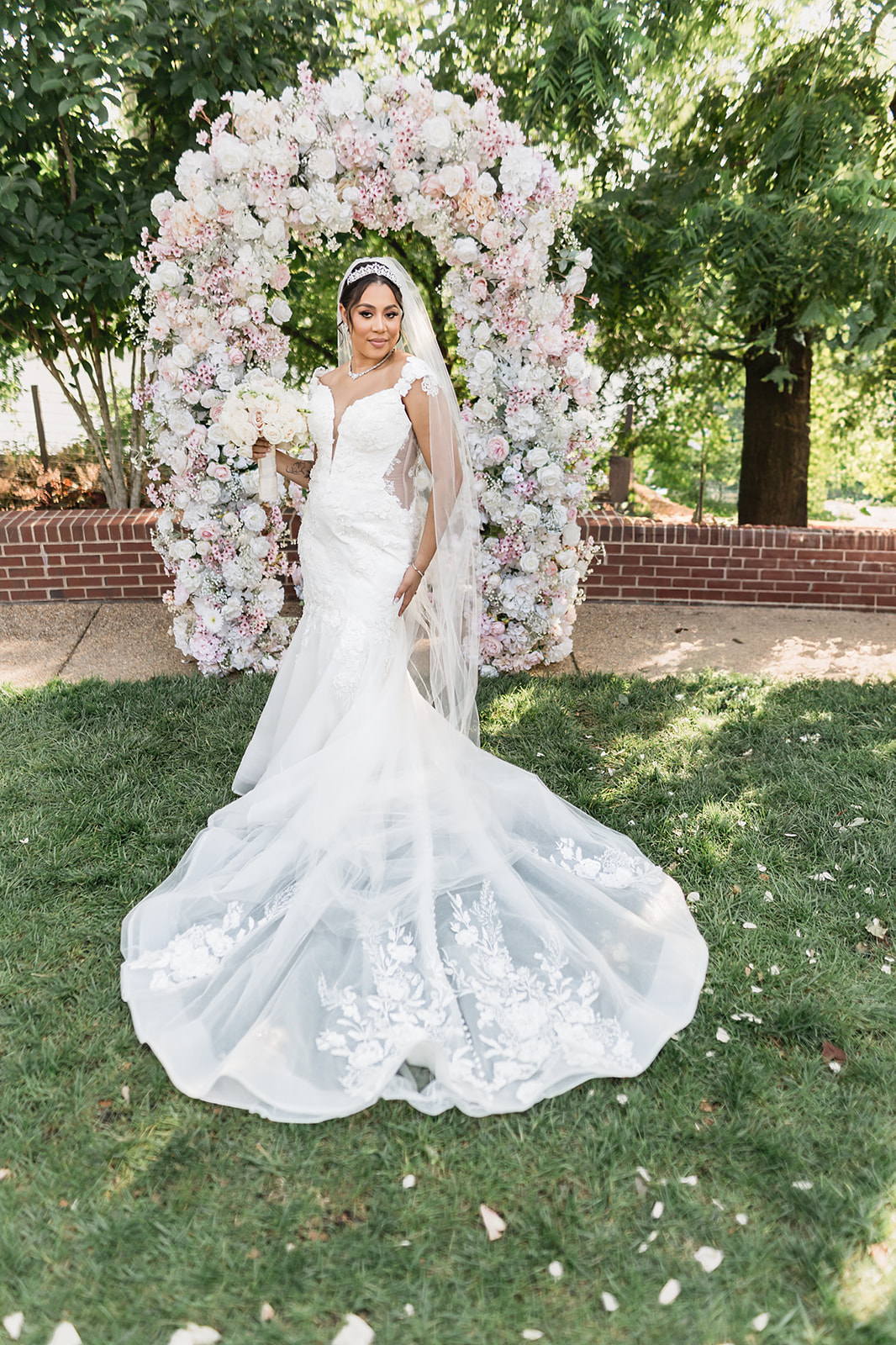 Bride in mermaid gown with tiara under pink and white floral arch garden