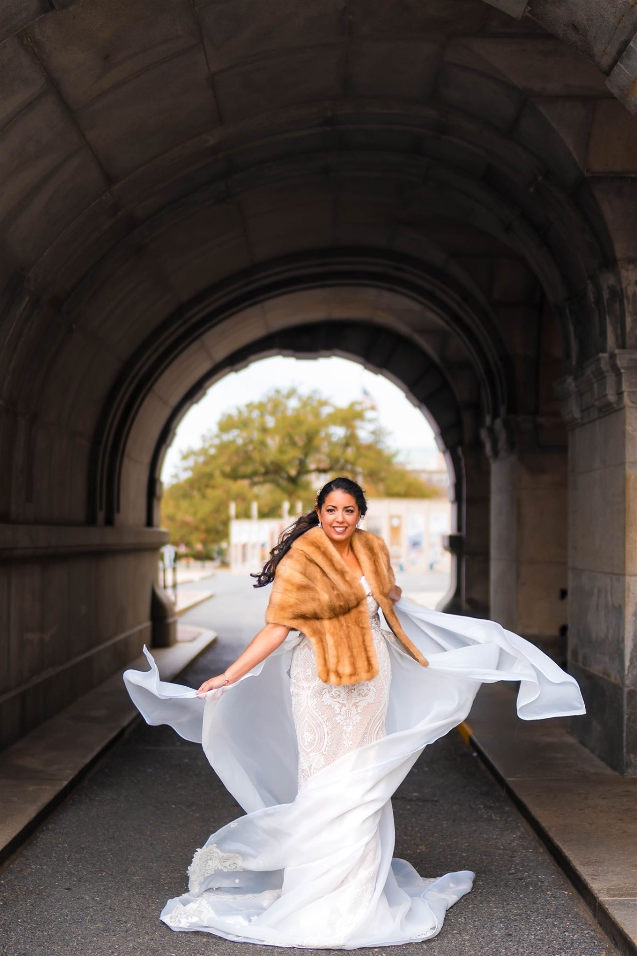 Bride in fur stole twirling gown stone archway editorial