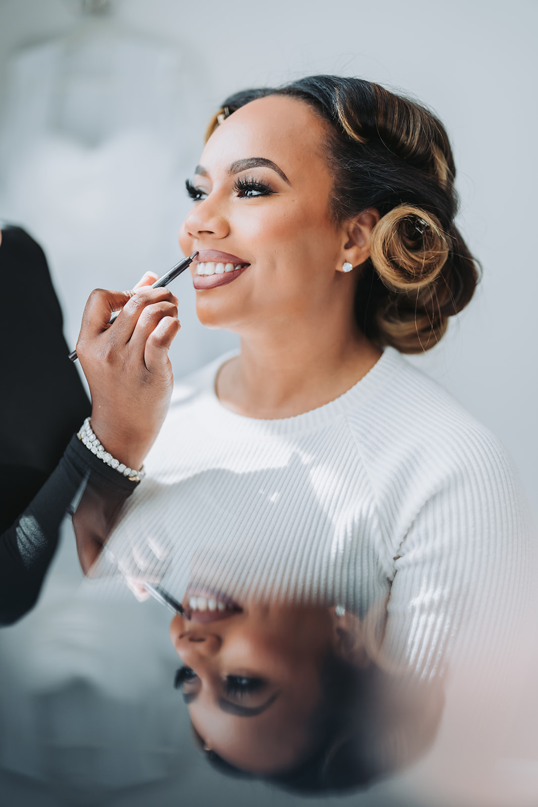 Bride getting makeup with mirror reflection smiling