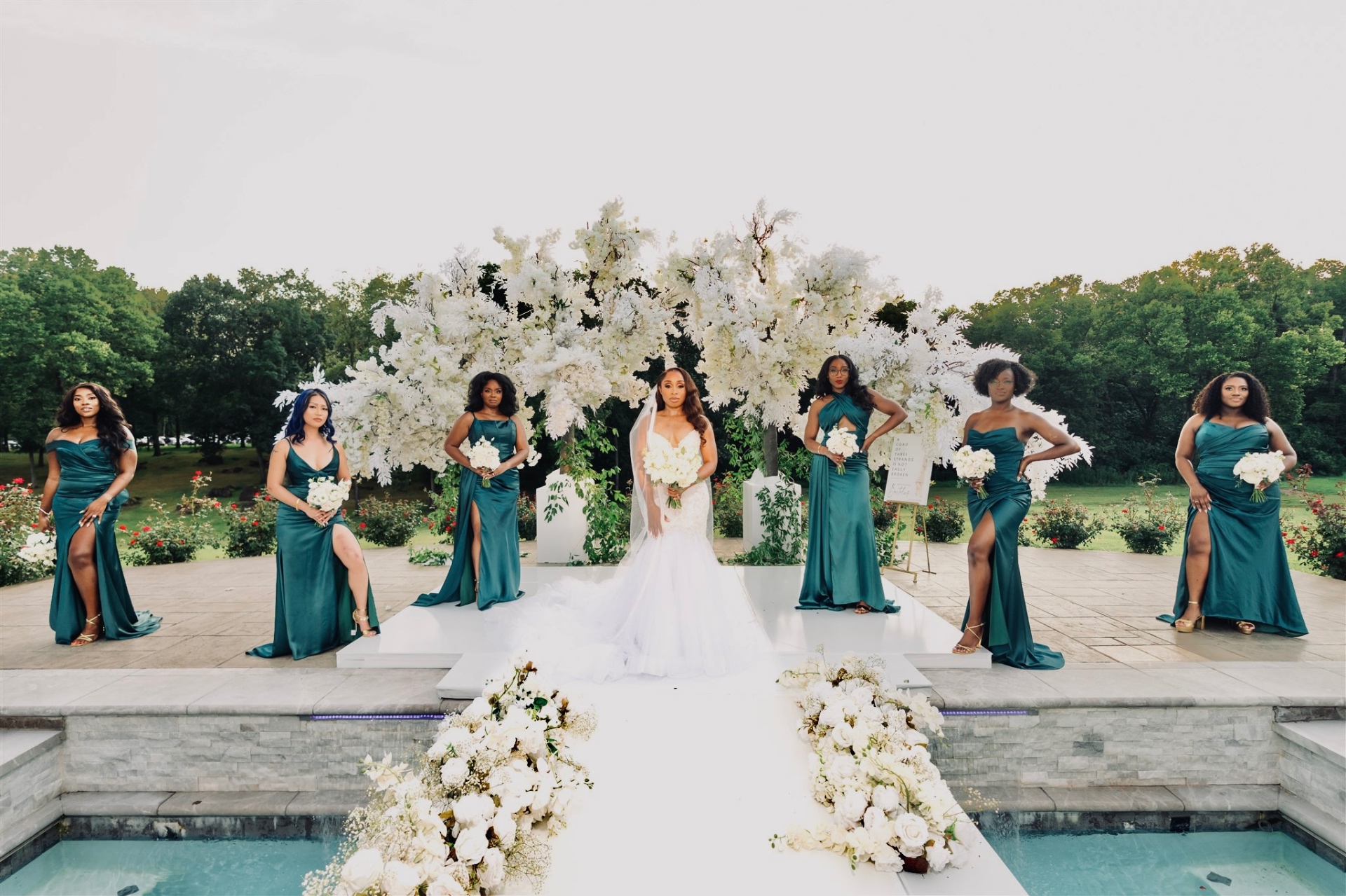 Bride with bridesmaids in teal gowns at floral arch poolside ceremony