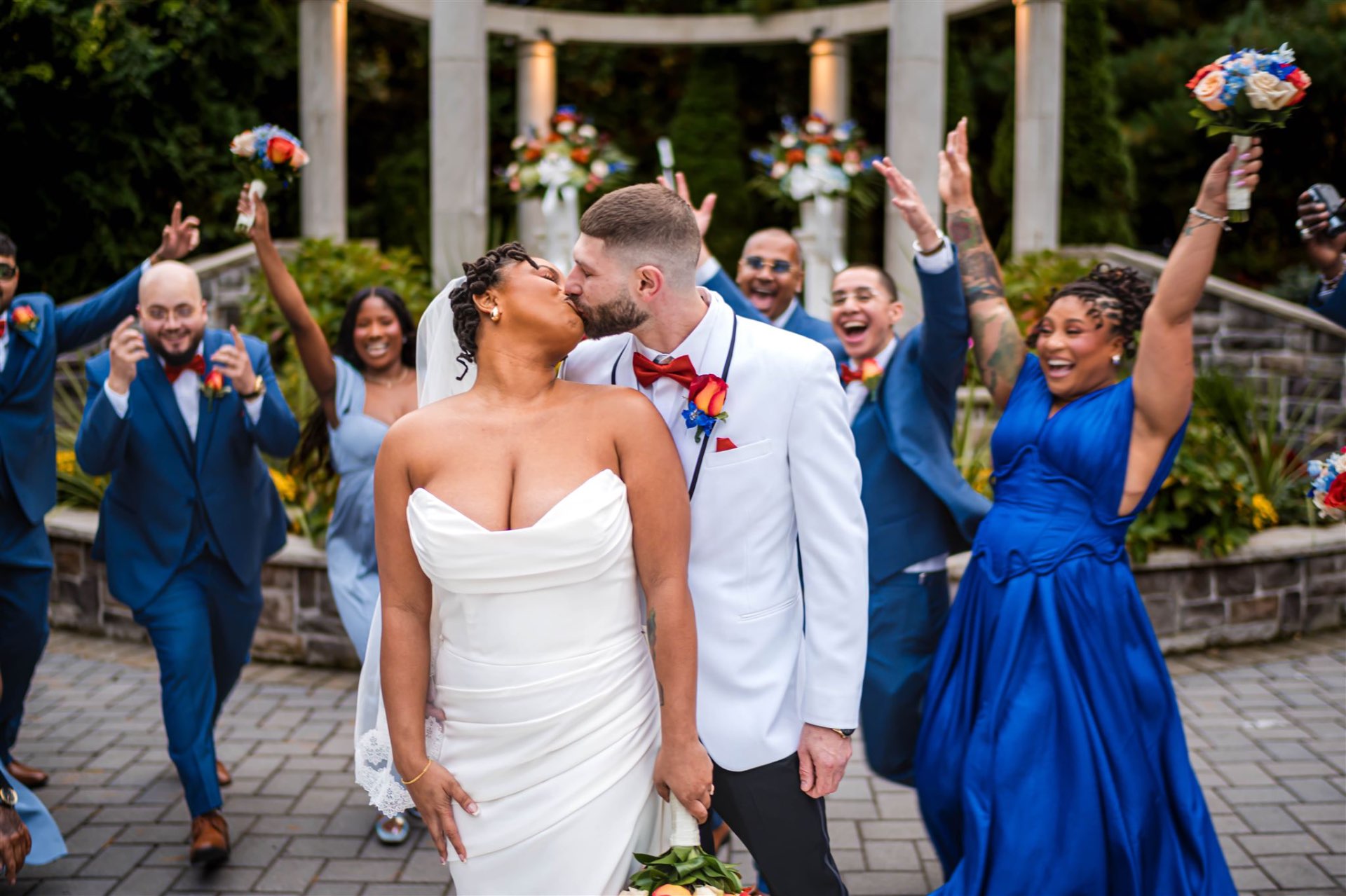 Couple kiss with bridal party celebrating at gazebo