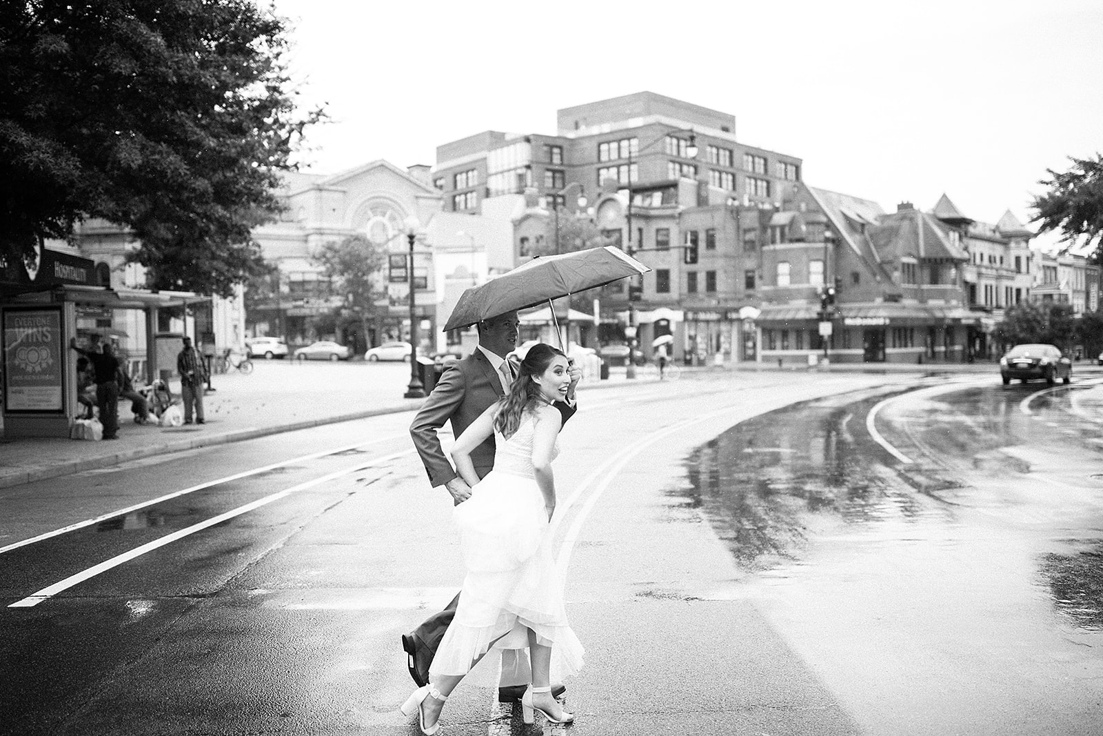 Couple crossing rainy city street with umbrella black and white candid