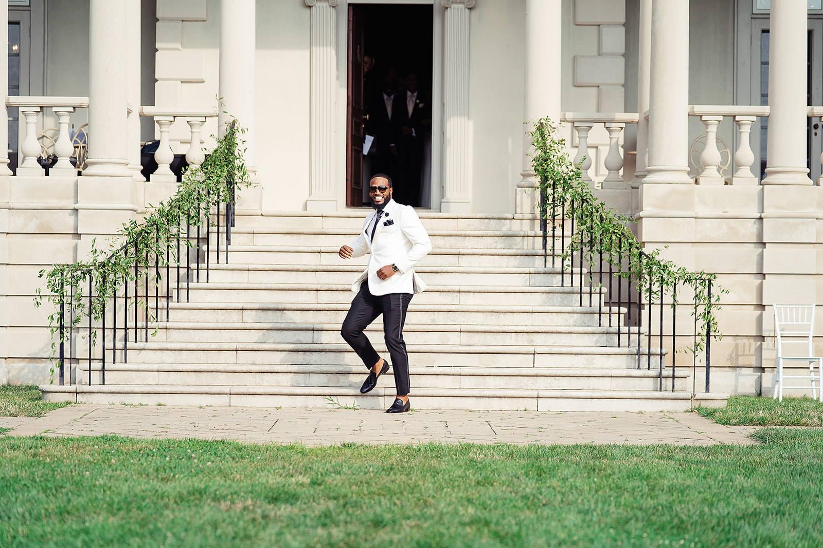 Groom confident entrance down mansion steps white jacket sunglasses