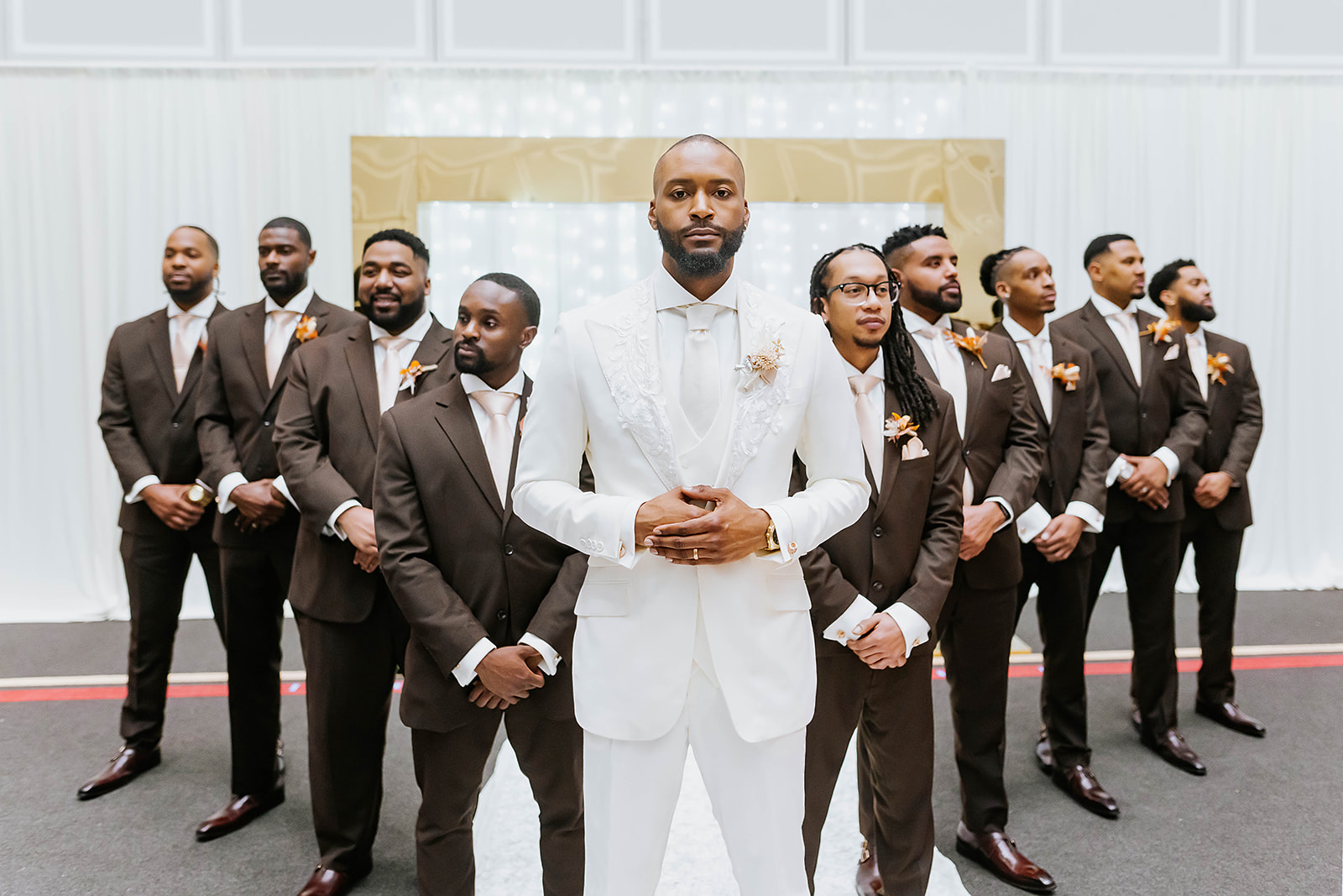 Groom in white suit with groomsmen in brown suits V formation